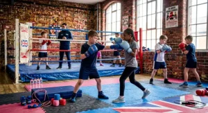 A group of diverse British primary school children participating in a junior boxing club training session.