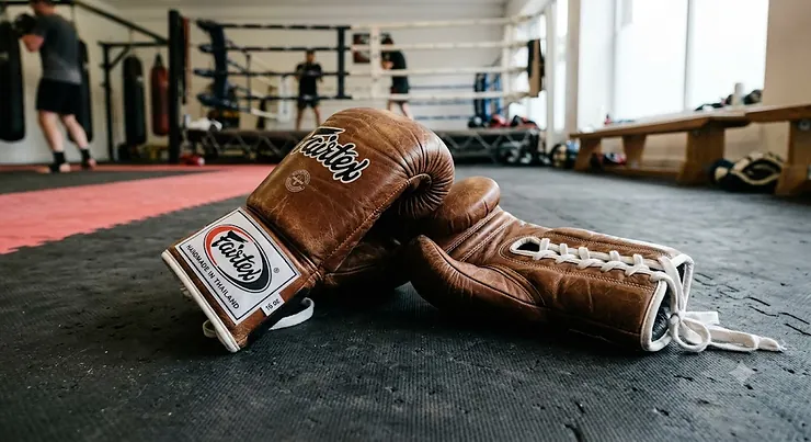 A pair of classic brown leather Fairtex boxing gloves on a gym mat, popular for Muay Thai training in the UK.
