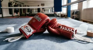 Red lace-up Fairtex boxing gloves laid out on a ring canvas before a professional bout.