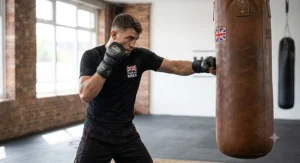 A British martial artist wearing ergonomic gloves for MMA sparring whilst striking a heavy bag in a local gym.