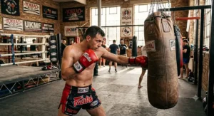 A fighter wearing red hook-and-loop Muay Thai gloves whilst training in a British combat sports gym.